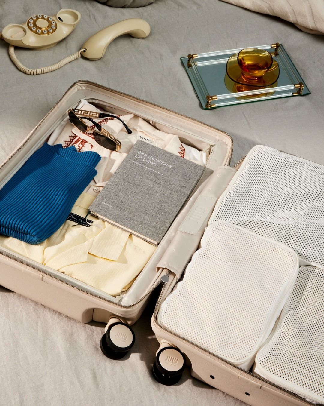 Open cream suitcase with packing cubes, folded clothes, and bedside travel details