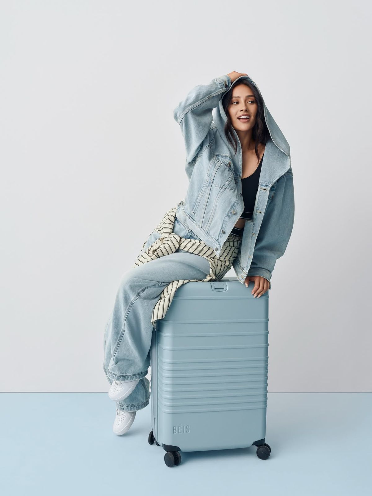 Woman in denim sitting on a pale blue suitcase