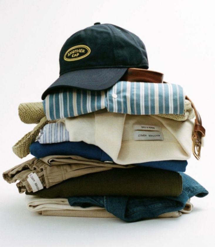 Folded travel clothes stacked with a black cap on top